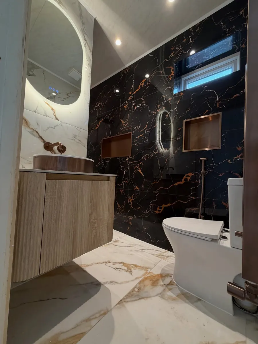 Floating oak vanity and copper wall niches in a marble-tiled bathroom